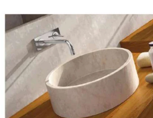 Photographie d'une vasque cylindrique en pierre claire posée sur un plan en bois, avec un robinet mural au-dessus